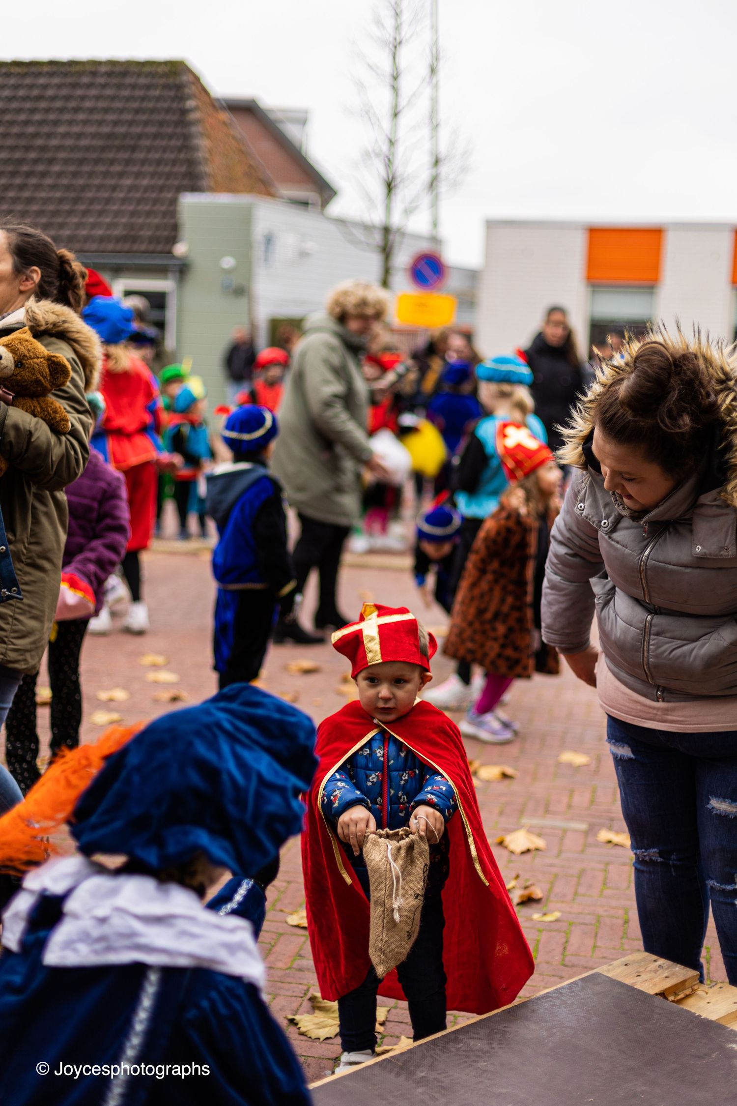 Children in colorful winter clothing and capes celebrate at an outdoor community event in cold weather.
