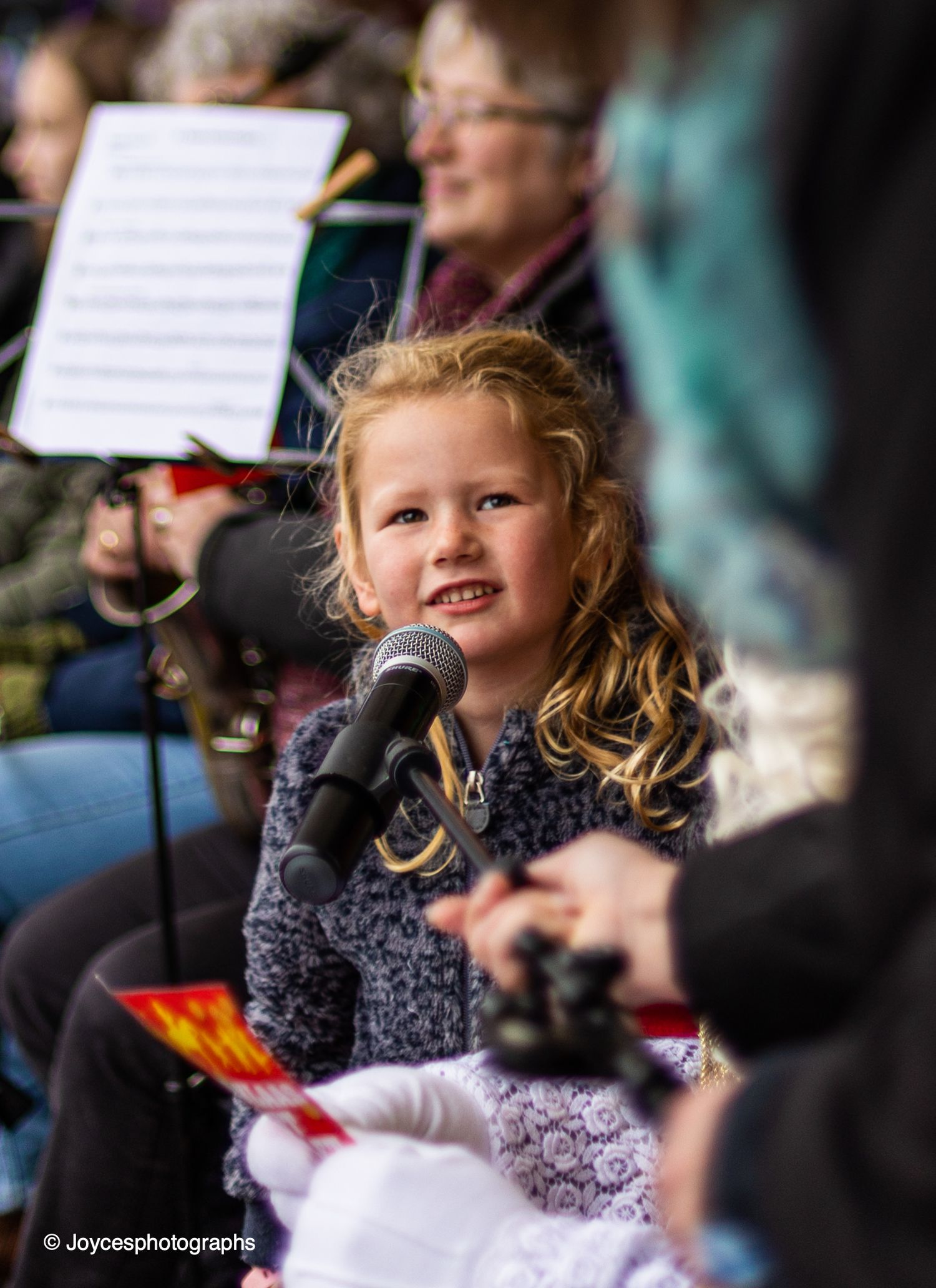 Young performer singing into microphone during live performance with sheet music visible in background.