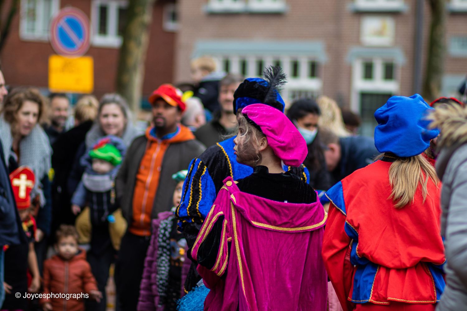 Spectators wearing colorful coats and hats line up along a street during an outdoor event.