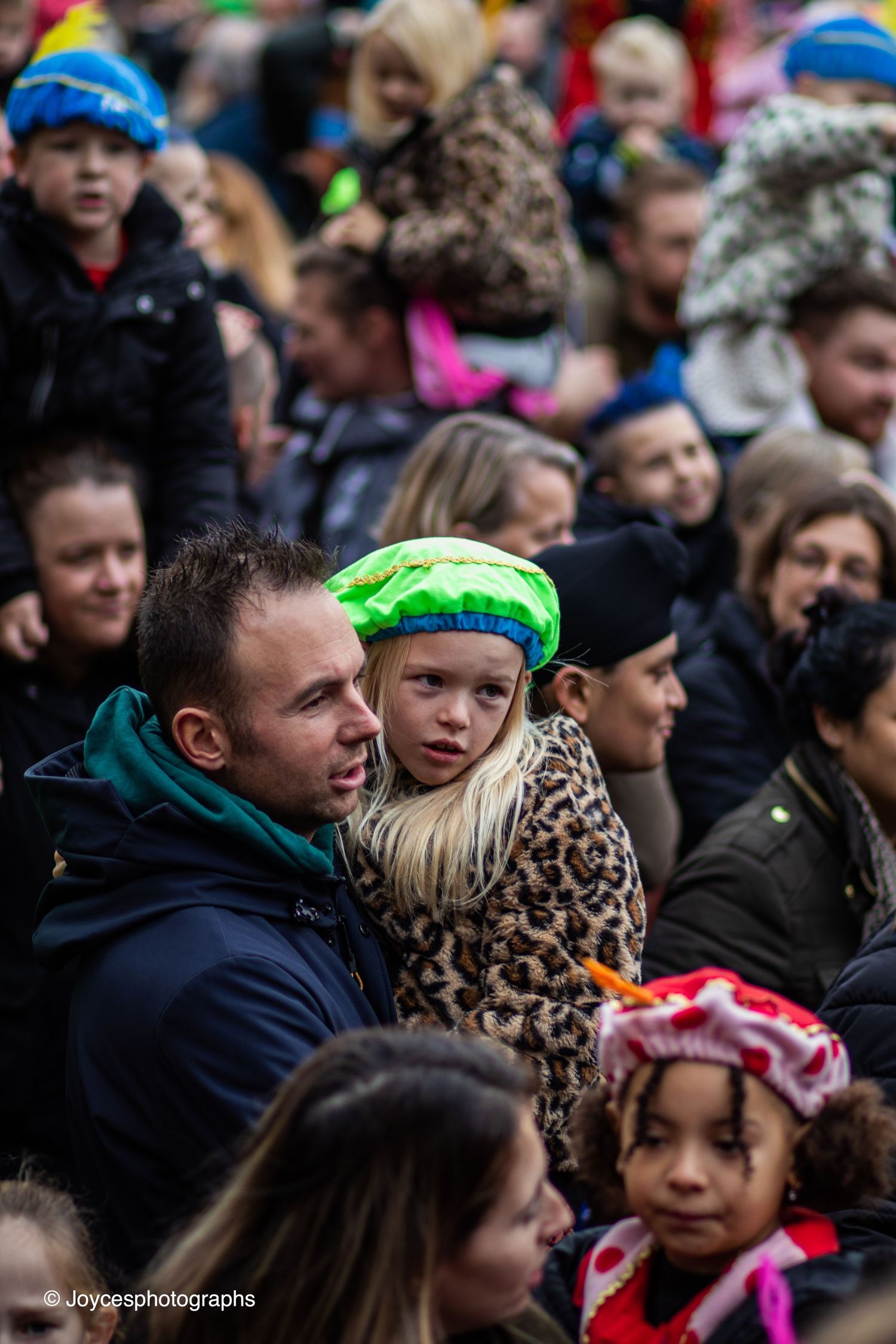 A crowd of spectators watches an event with colorful headbands and accessories visible in the frame.