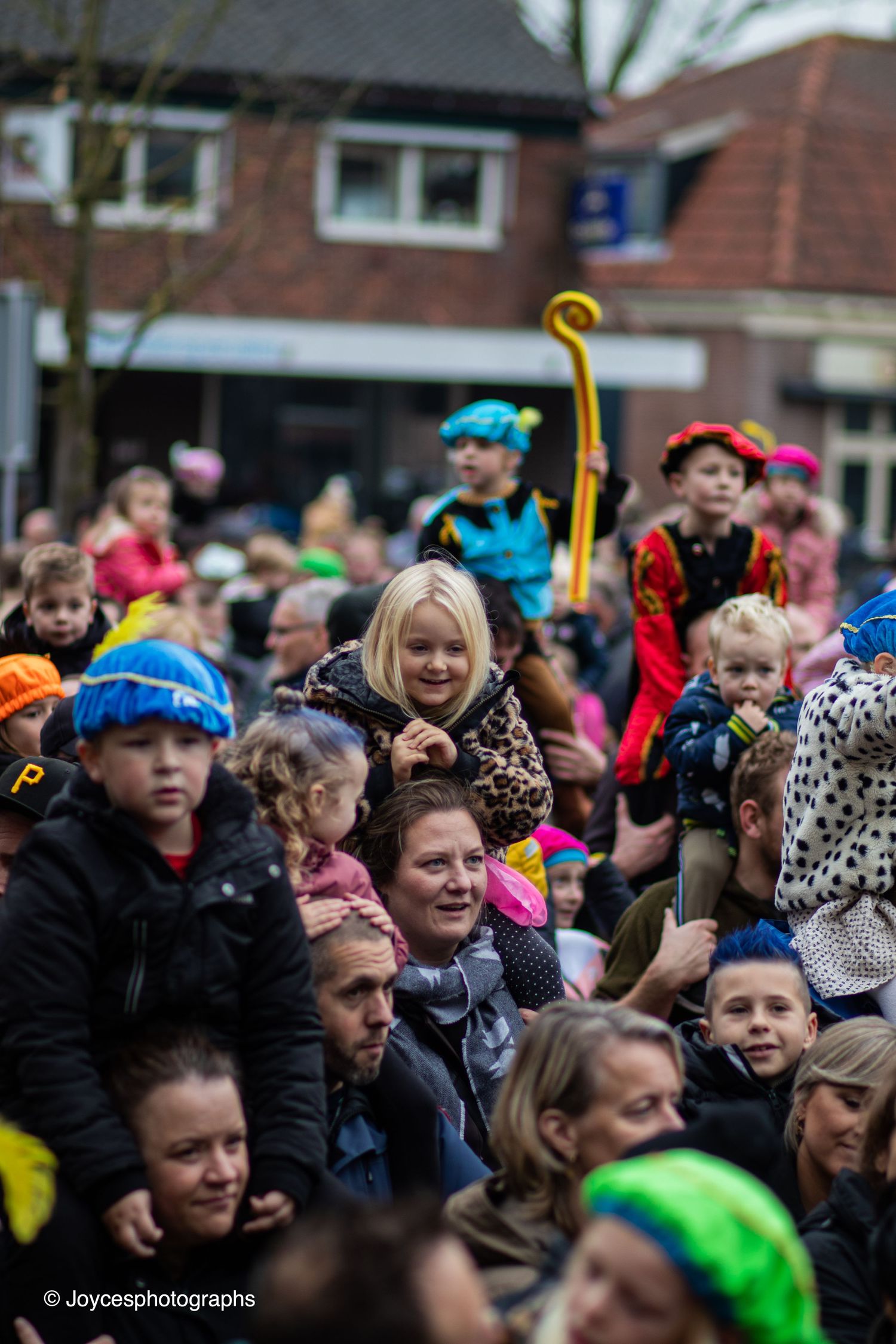 A crowd of excited spectators at an outdoor event cheering and waving with colorful accessories and clothing.