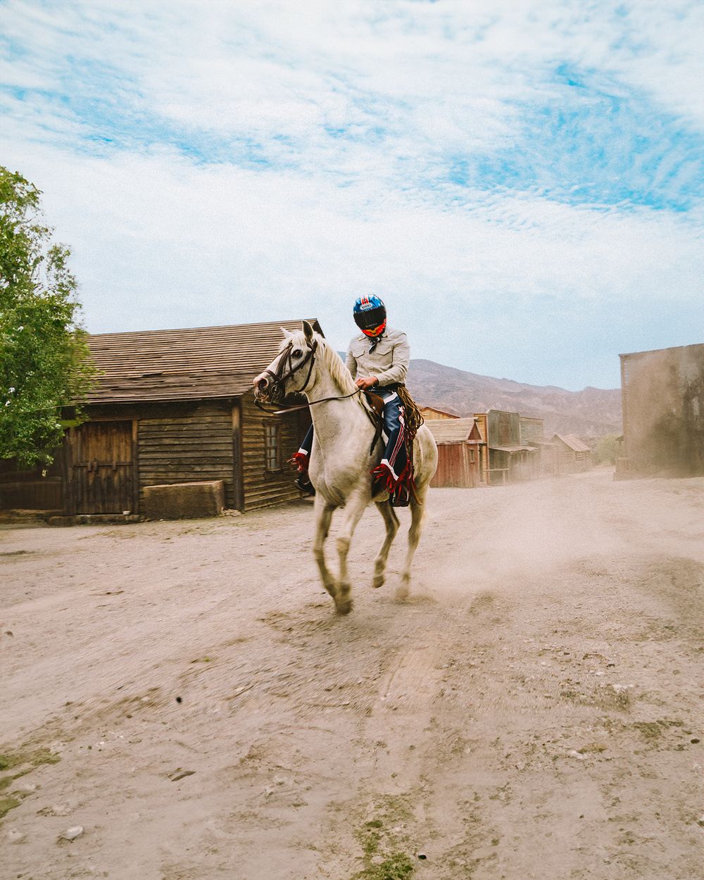 A rider on a white horse kicks up dust while practicing in a rustic arena during a training session.