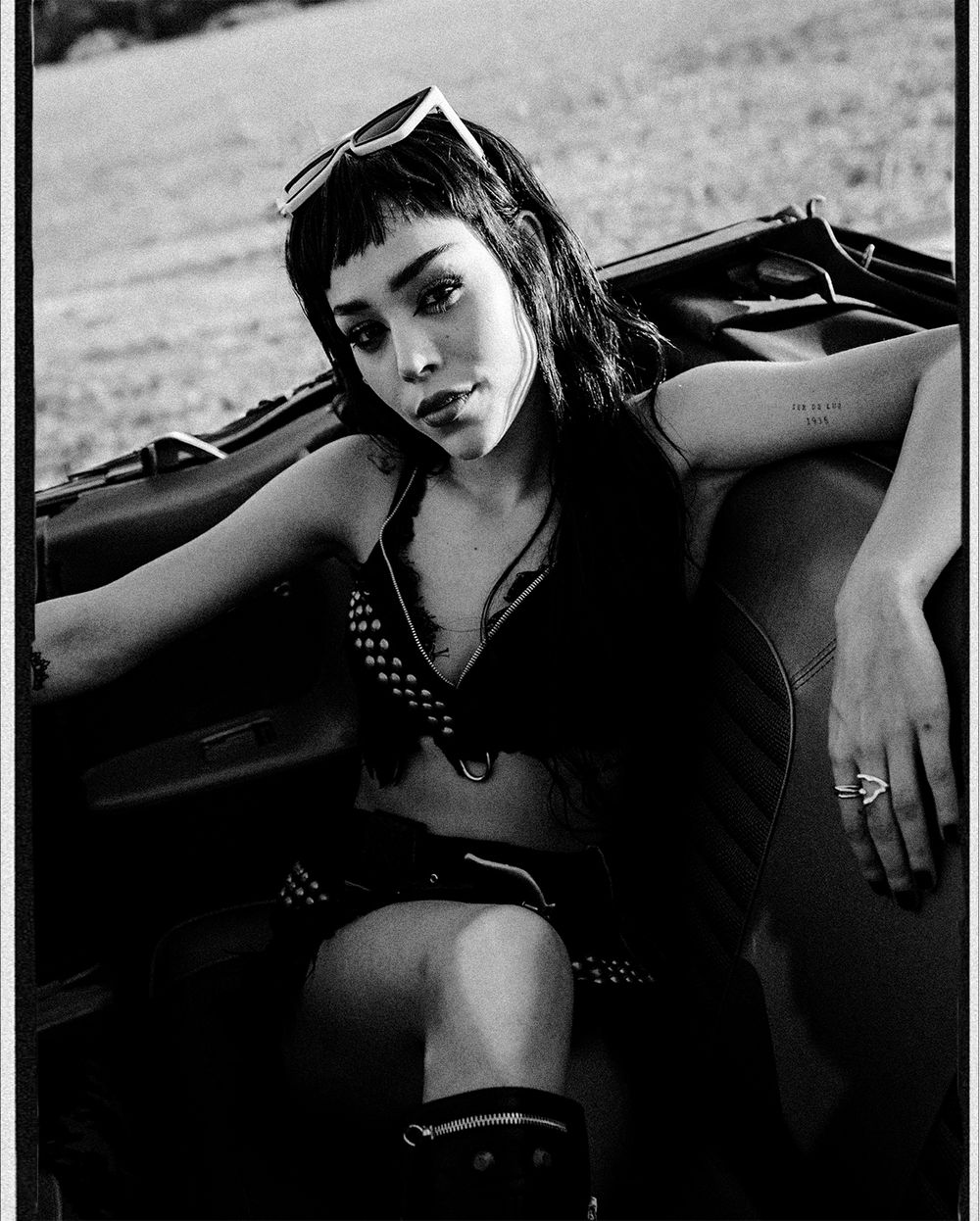 Artistic black and white fashion photo series showing model in dark outfit reclining against car interior.