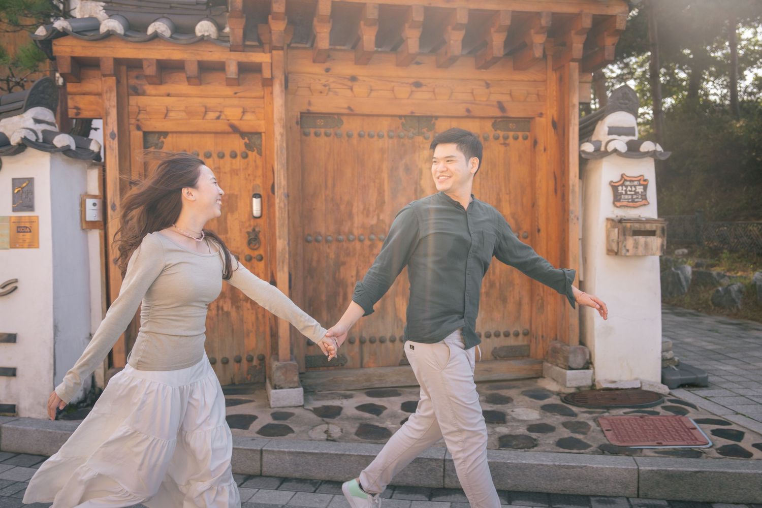 A couple in traditional Korean hanbok attire poses together at a historic temple during sunset.