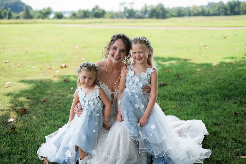 Two young children in matching blue and white dresses play together in a sunny green field.