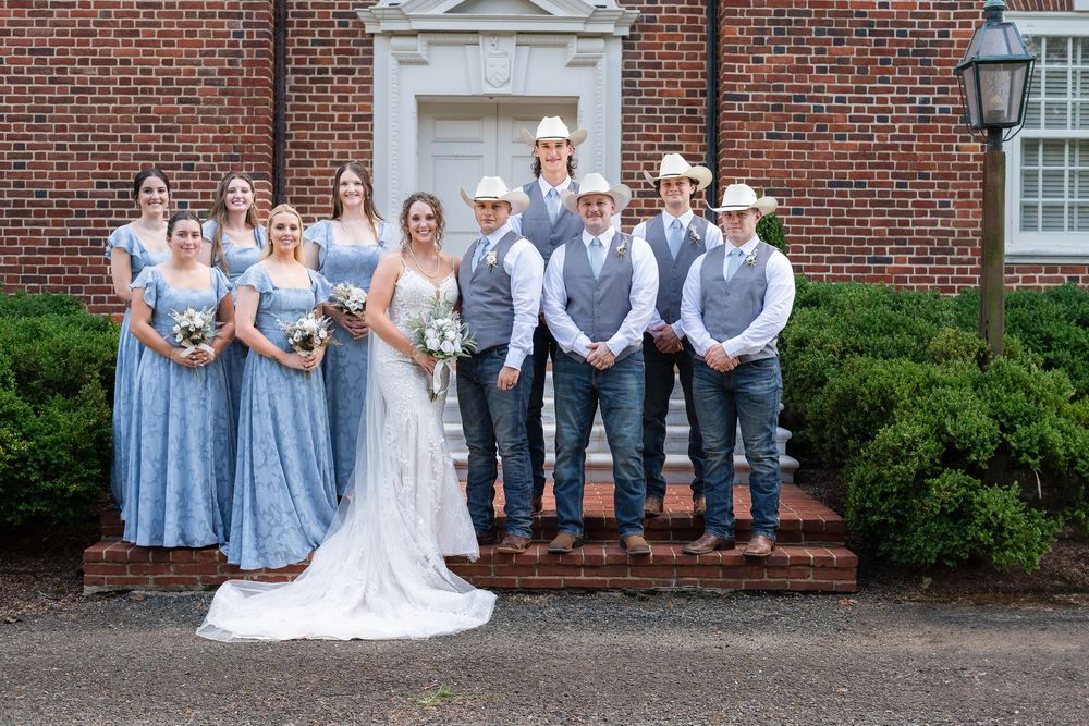 Wedding party in blue dresses and gray suits poses in front of red brick building with white columns.