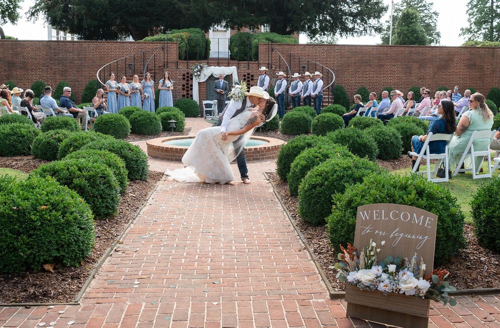 A couple shares their first dance at an outdoor garden wedding ceremony surrounded by manicured boxwood hedges and brick paths.