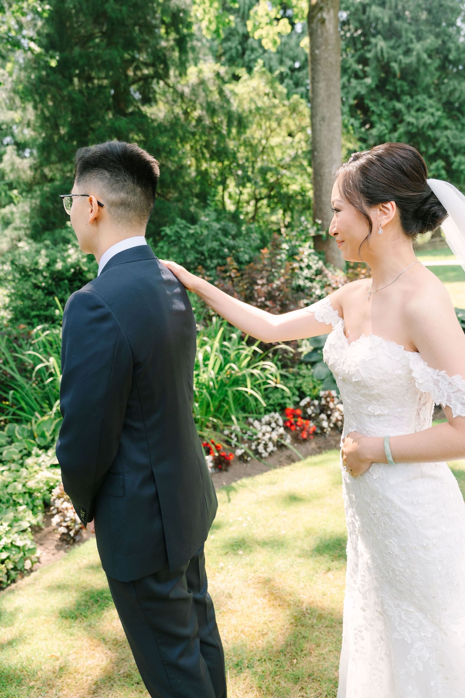 A wedding couple shares a playful first look moment in a sunny garden setting.