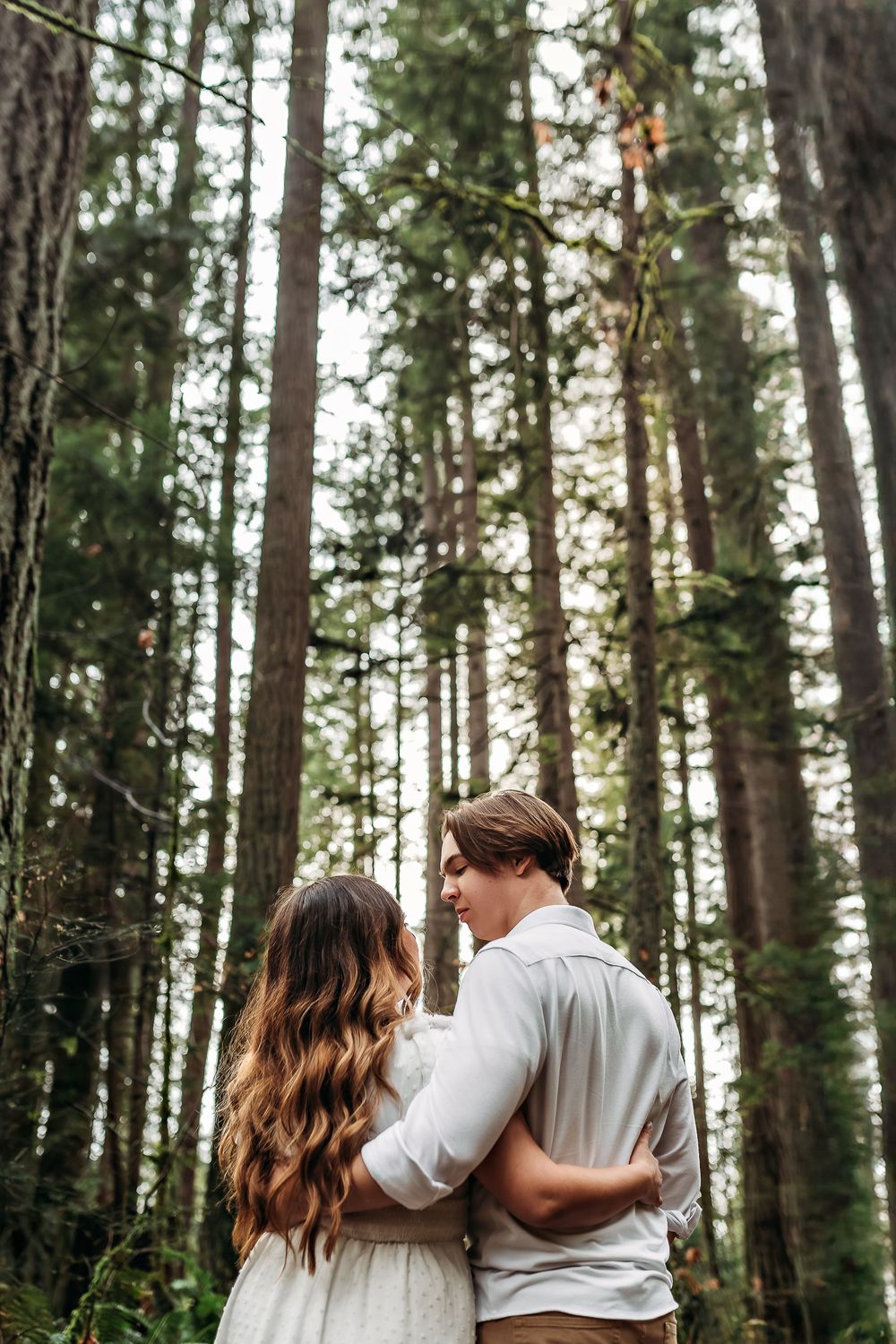 A tender moment captured between two people walking through a serene forest landscape.