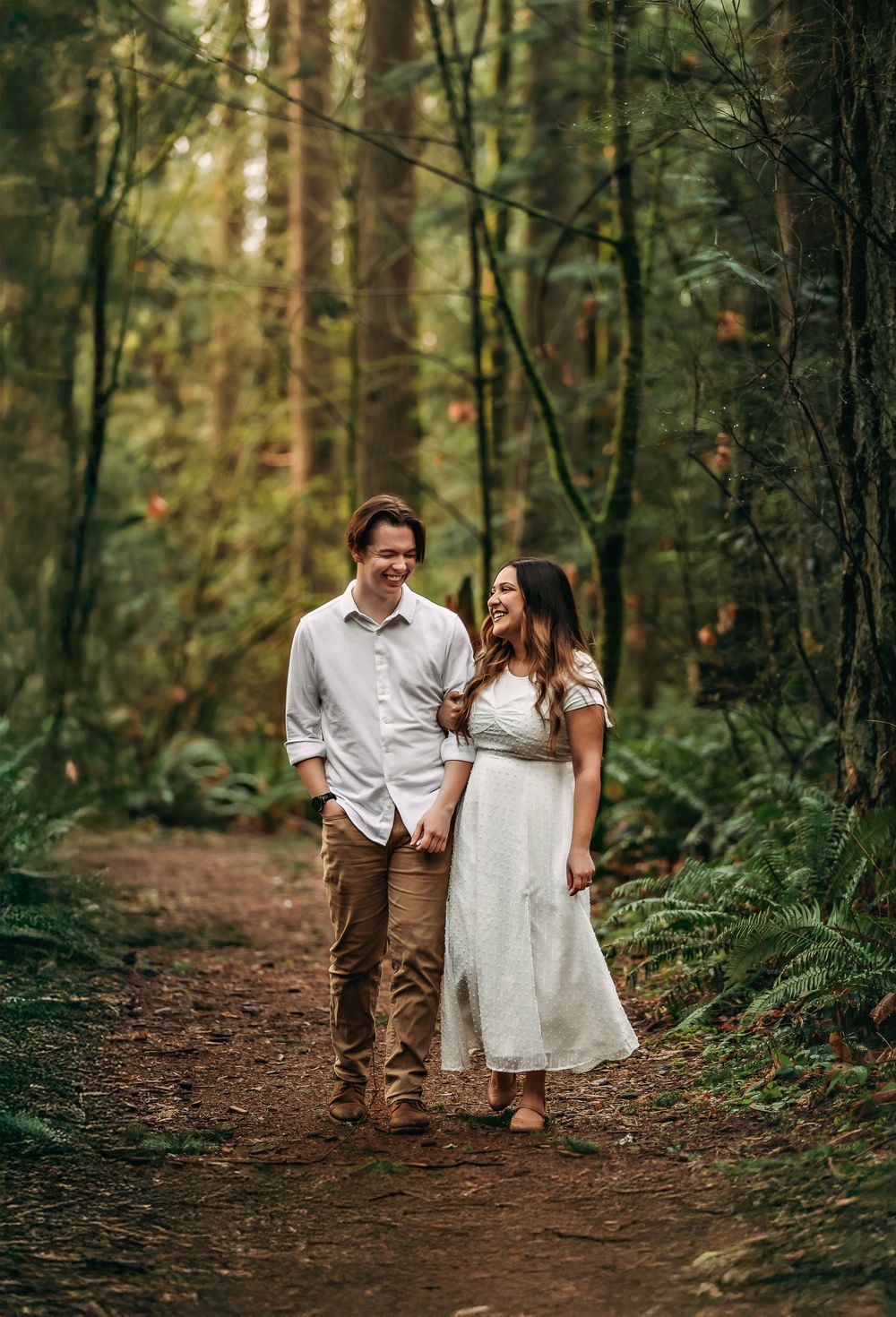 A couple strolls hand in hand along a winding forest trail surrounded by evergreens.