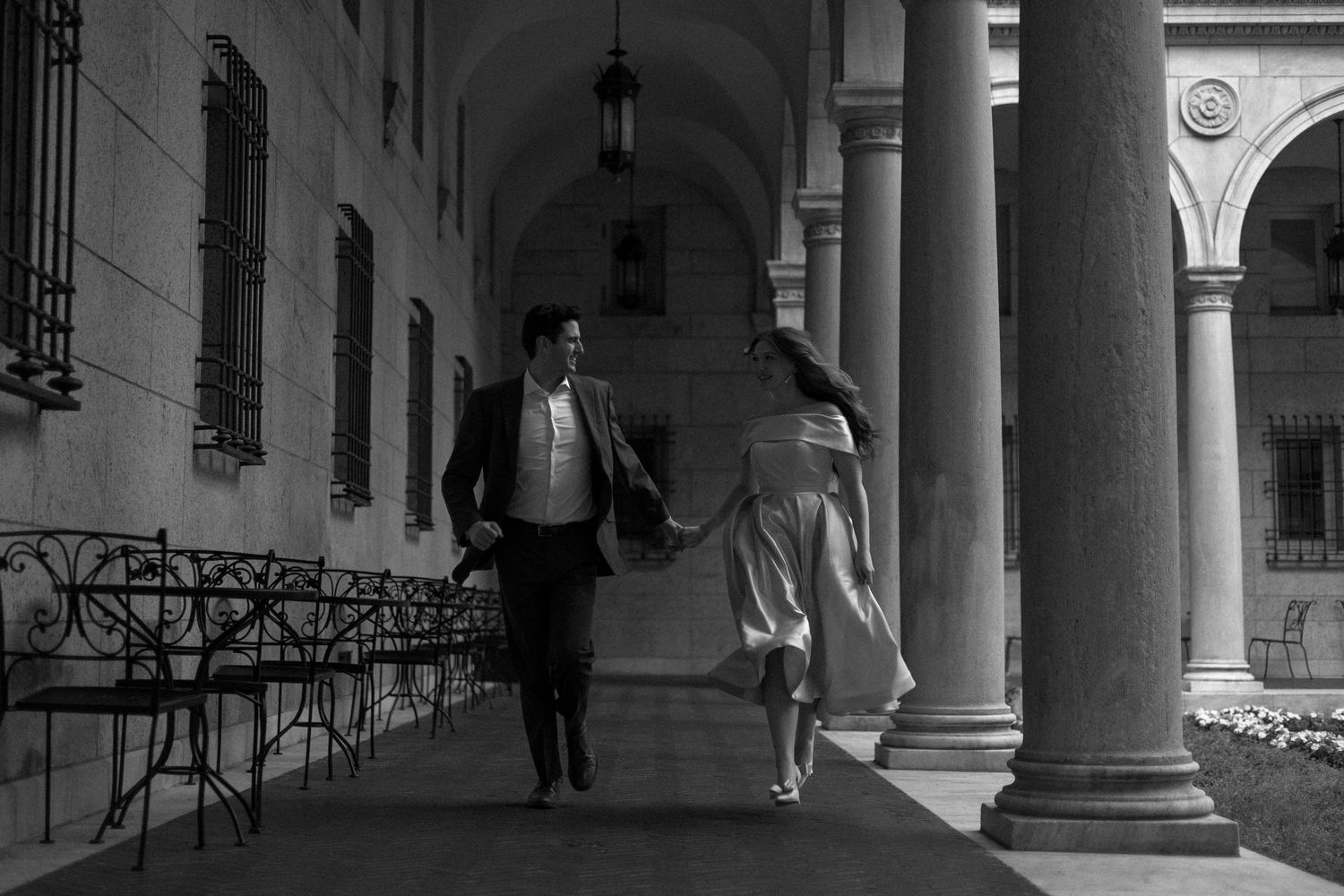 Art gallery hallway with white columns and black and white photographs hanging on walls in dramatic lighting.