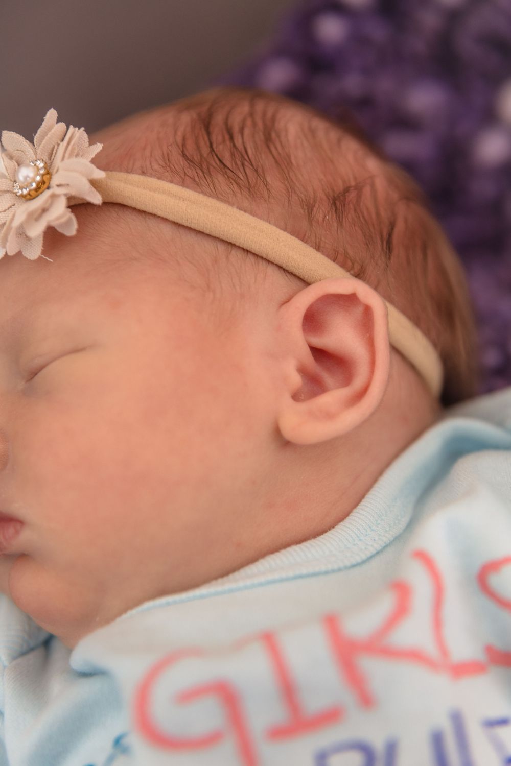 Sleeping newborn baby wearing a light blue outfit with text against purple background.