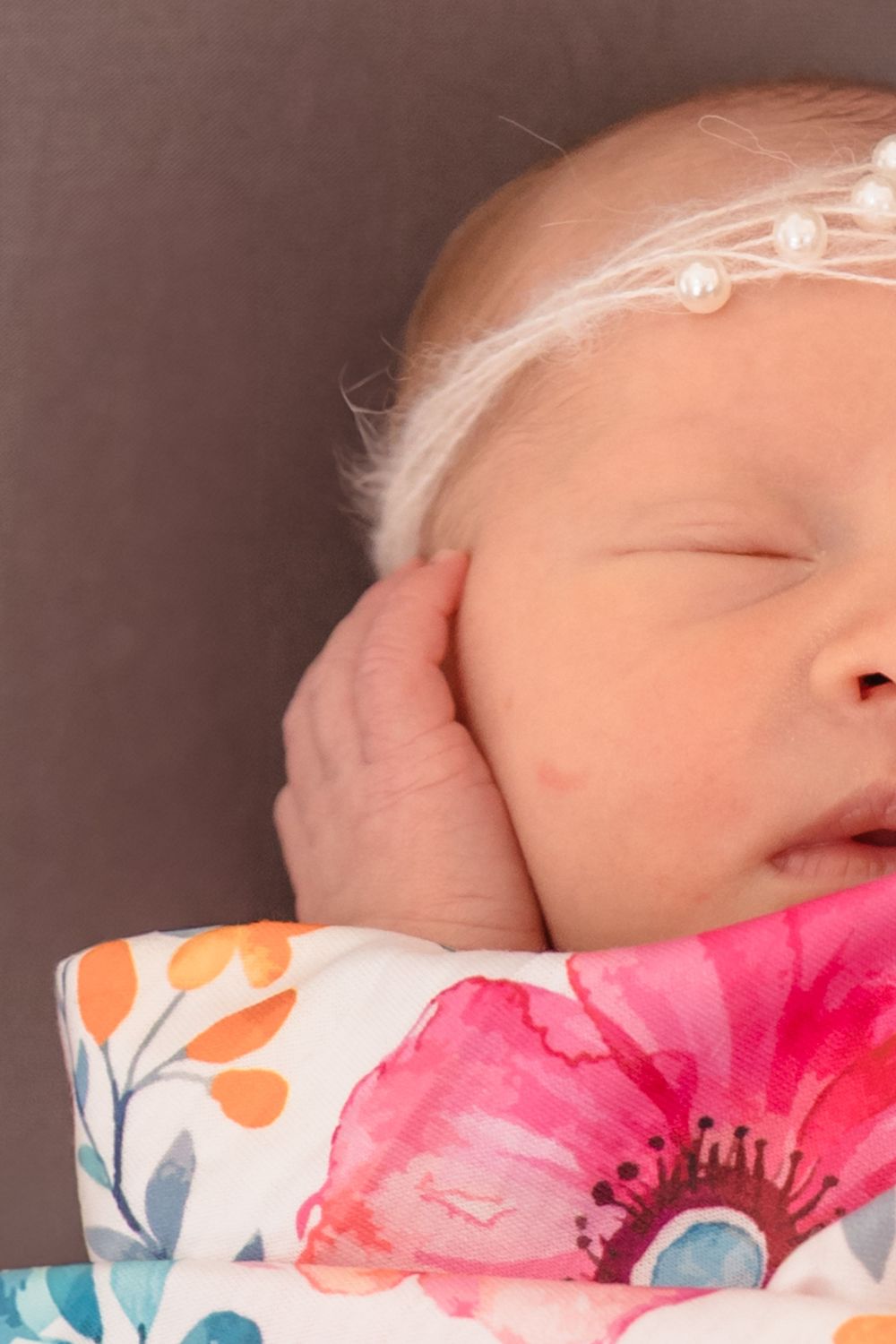 Sleeping newborn on floral print fabric with soft lighting and neutral background.