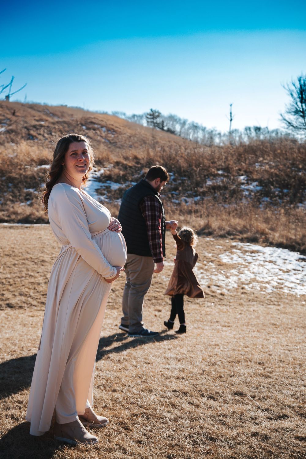 Family maternity photos taken on a hilltop with patches of snow visible.