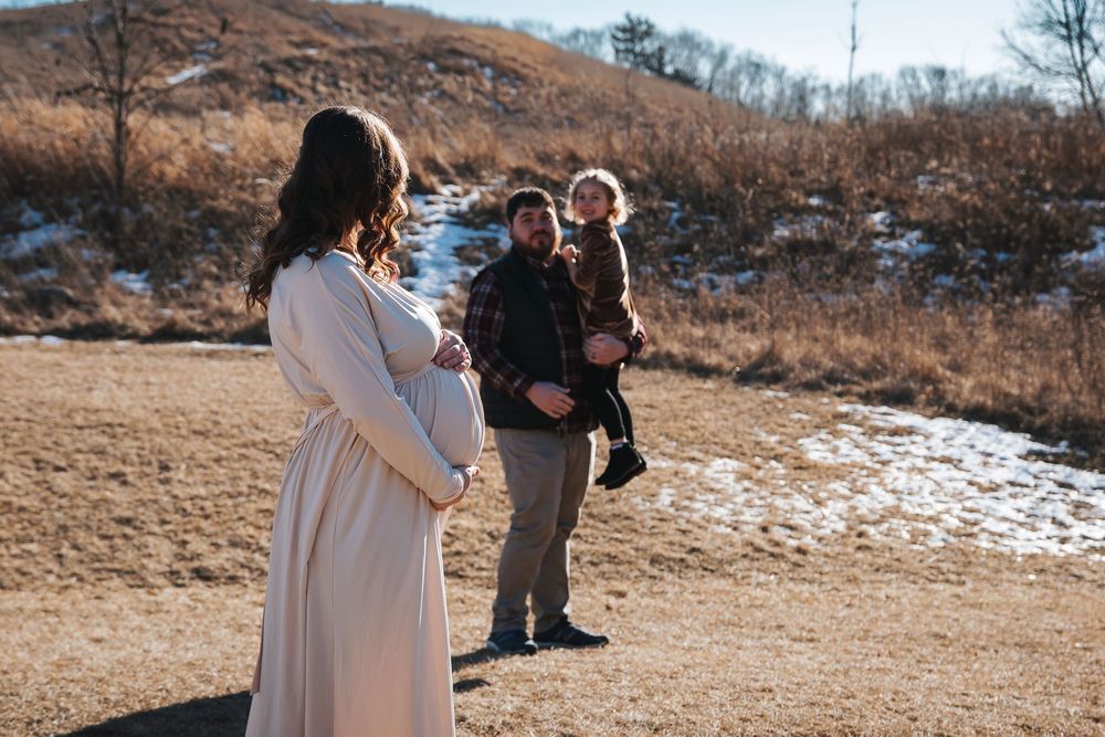 Winter maternity session featuring a flowing cream dress against brown grassy hills.