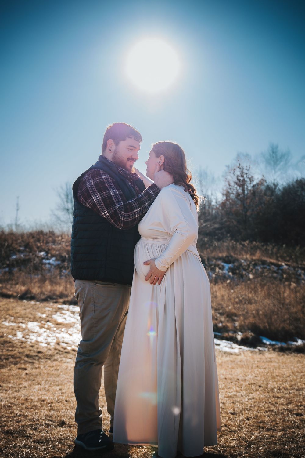 Maternity photoshoot in a snowy field at sunset with couple in casual winter attire.