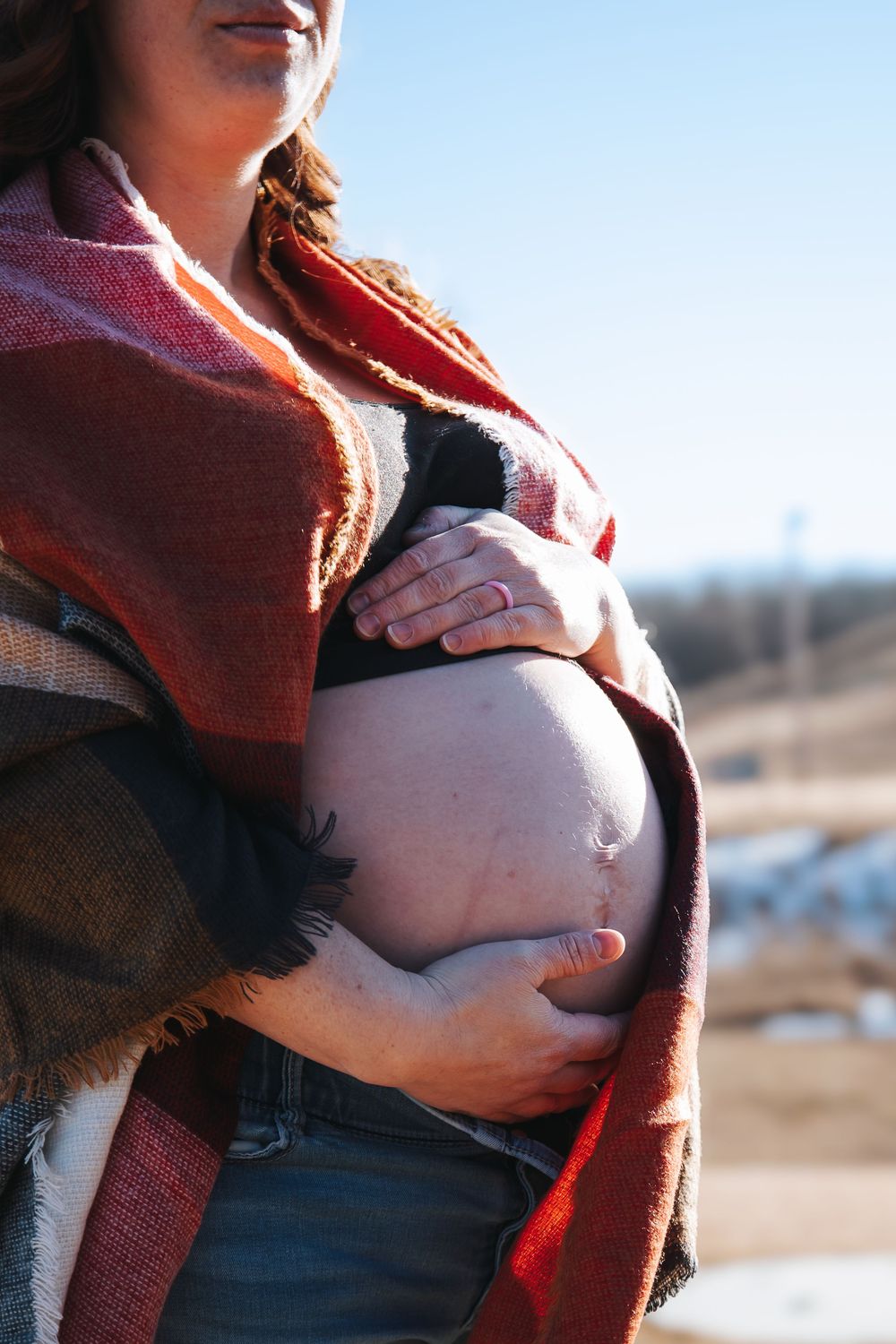 Sunlit maternity photo with hands tenderly placed on pregnant belly wearing red sweater.