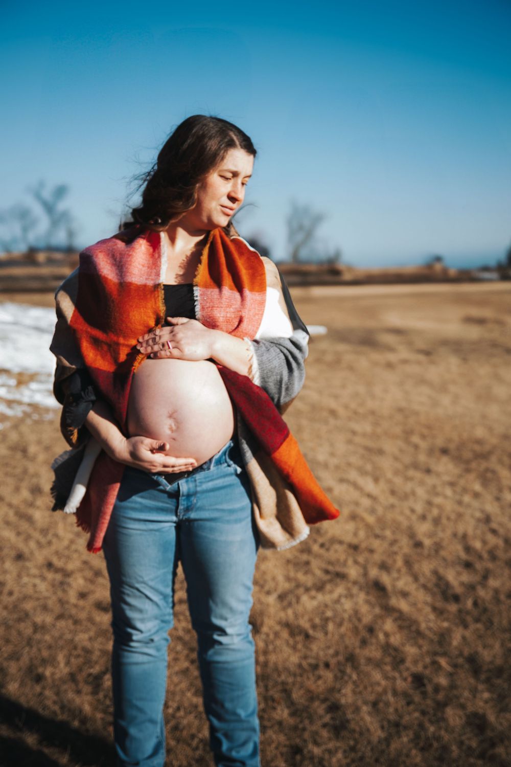 Outdoor maternity session showing pregnant belly against blue sky and winter landscape.