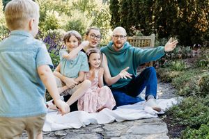 Family relaxing together on a stone wall in a garden with trees and flowers on a sunny day.