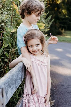 Two children share a sweet moment together while leaning against a wooden fence on a garden path.