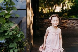 A sequence of five outdoor portraits of someone in a pink dress sitting near brick walls and greenery.