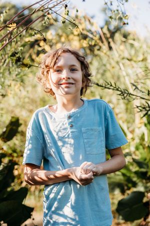 A child in a light blue t-shirt enjoys playing outside on a sunny day with trees and foliage in the background.