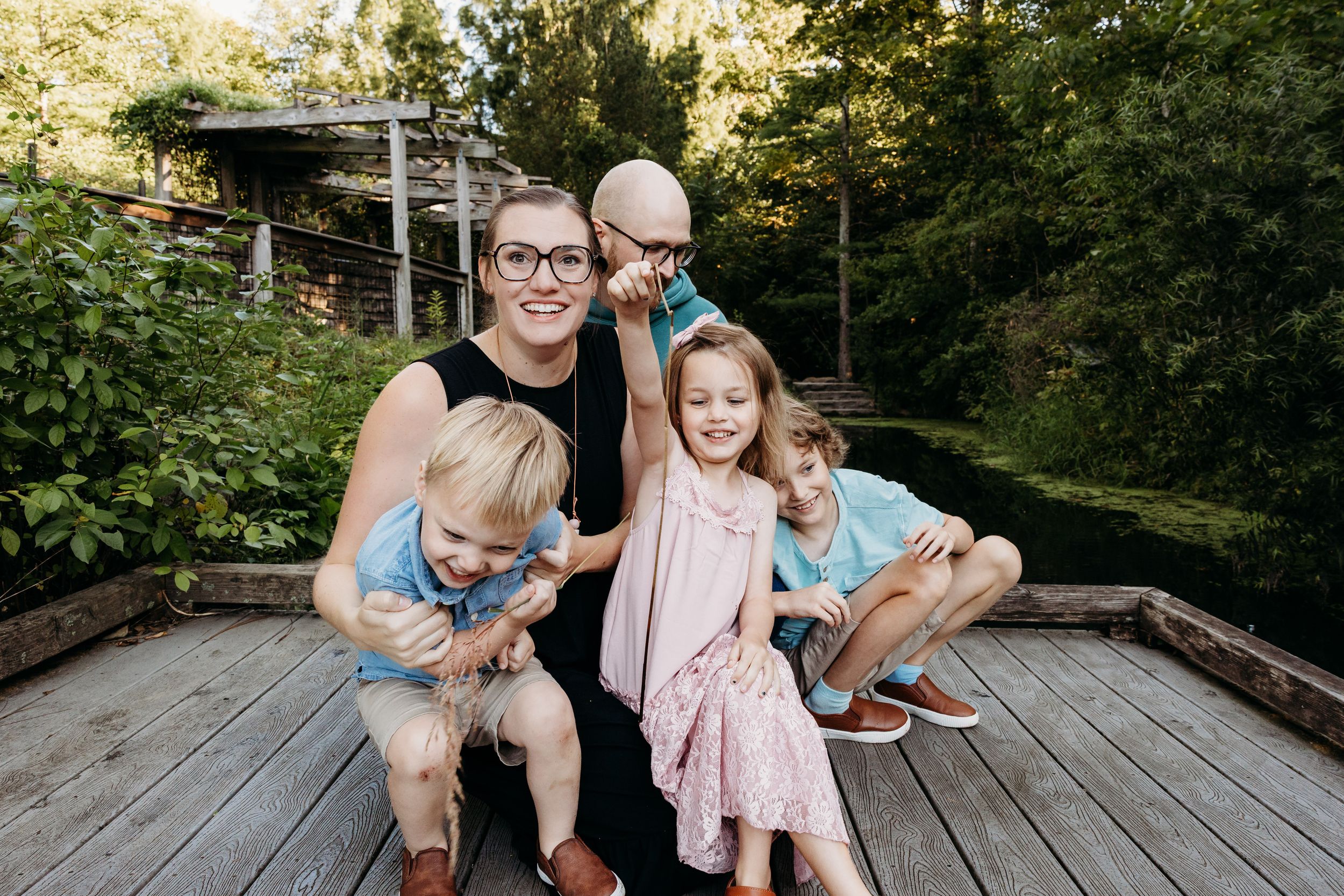 Family members share joyful laughter while sitting together on a rustic wooden deck surrounded by greenery.