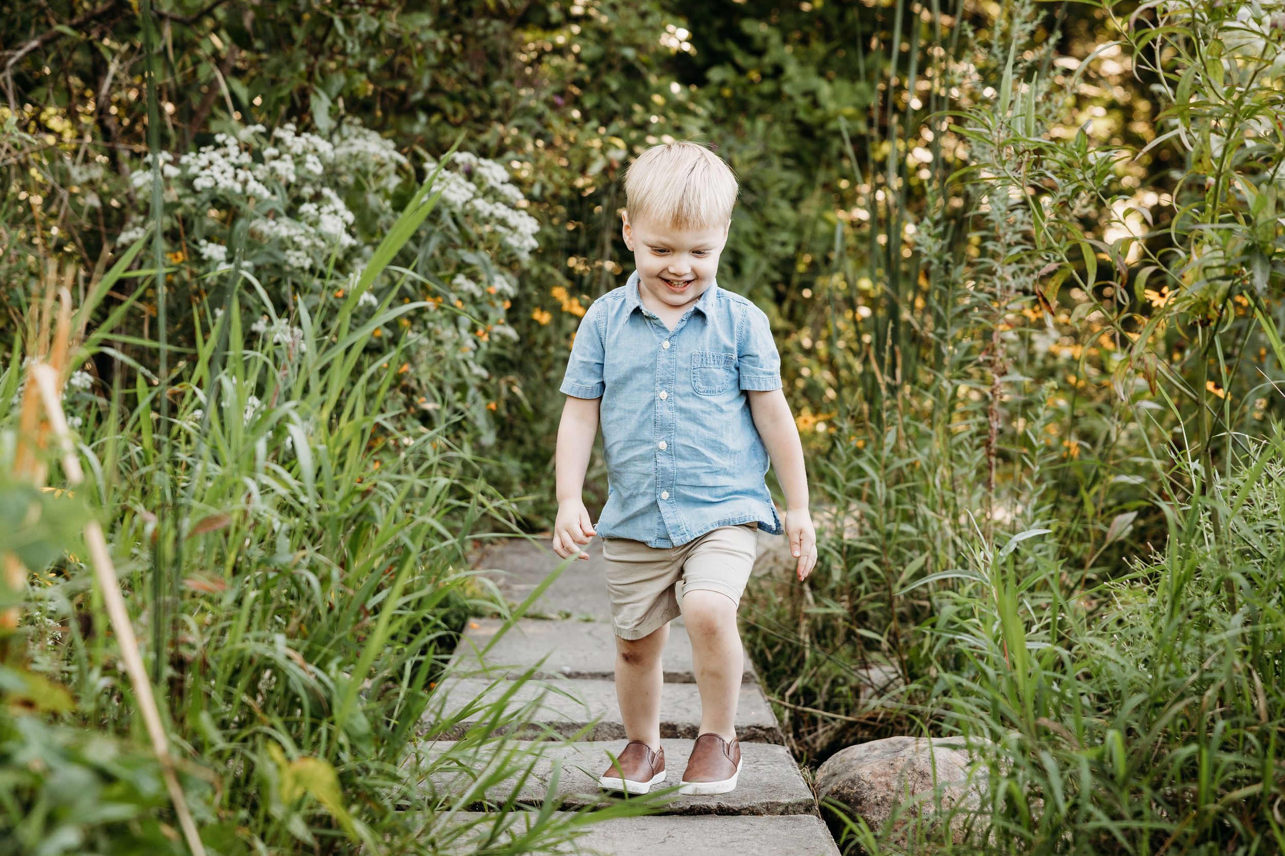 Toddlers sit on rocks and explore a lush garden with blooming flowers during a summer day.