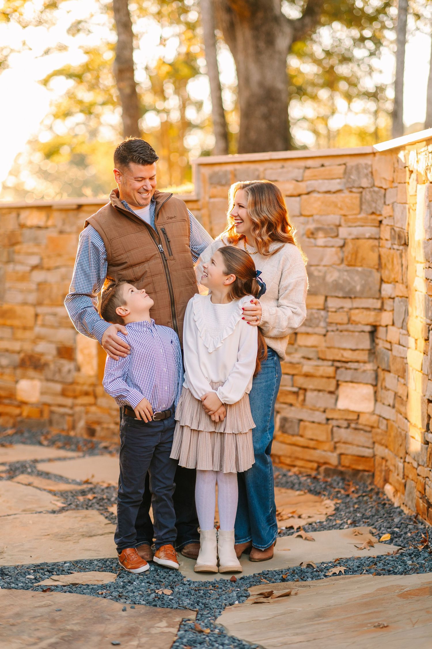 A family poses together against a stone wall during a golden sunset photo session outdoors.