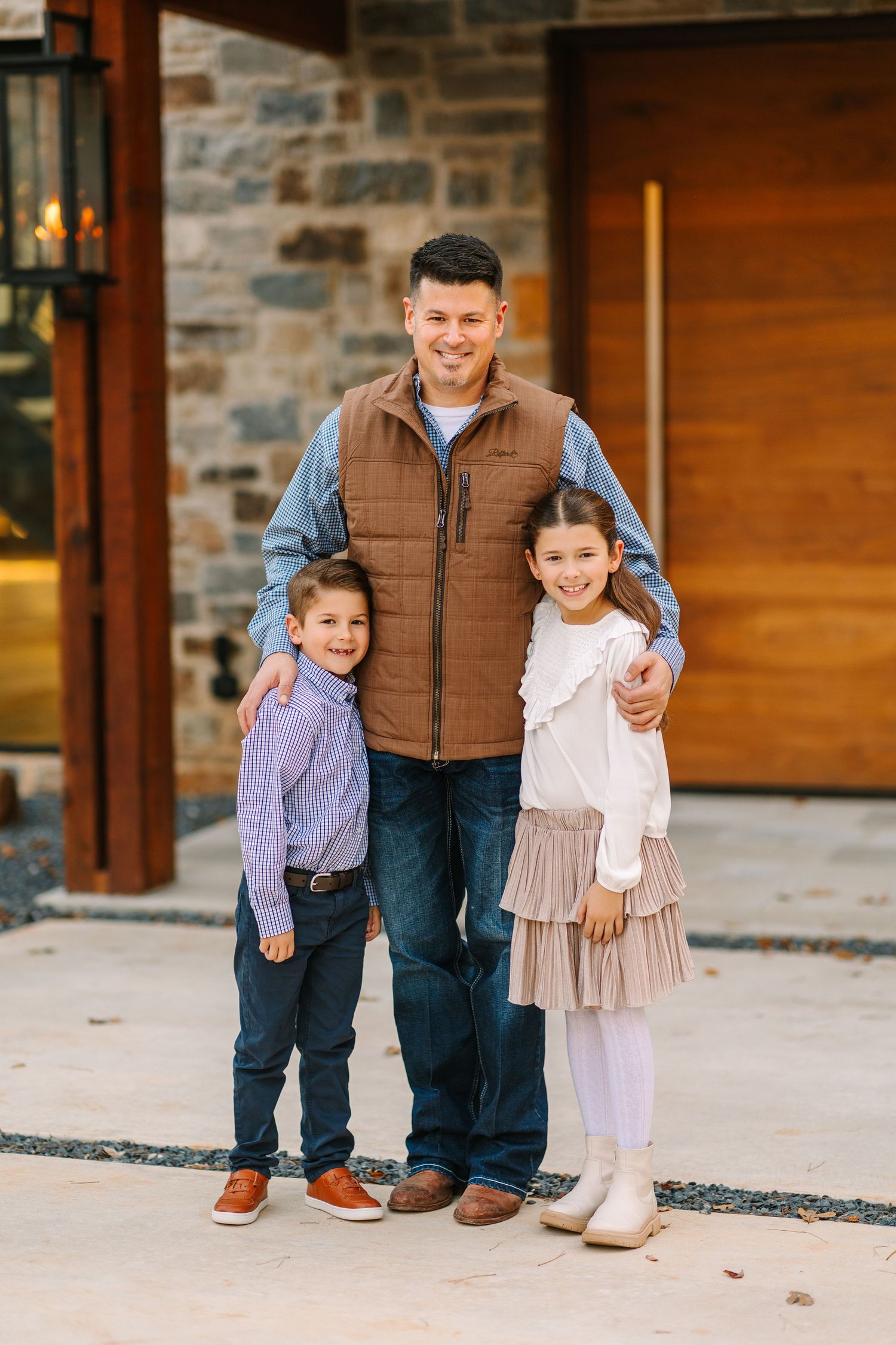 An outdoor portrait against stone and wood architecture shows a parent with two children.