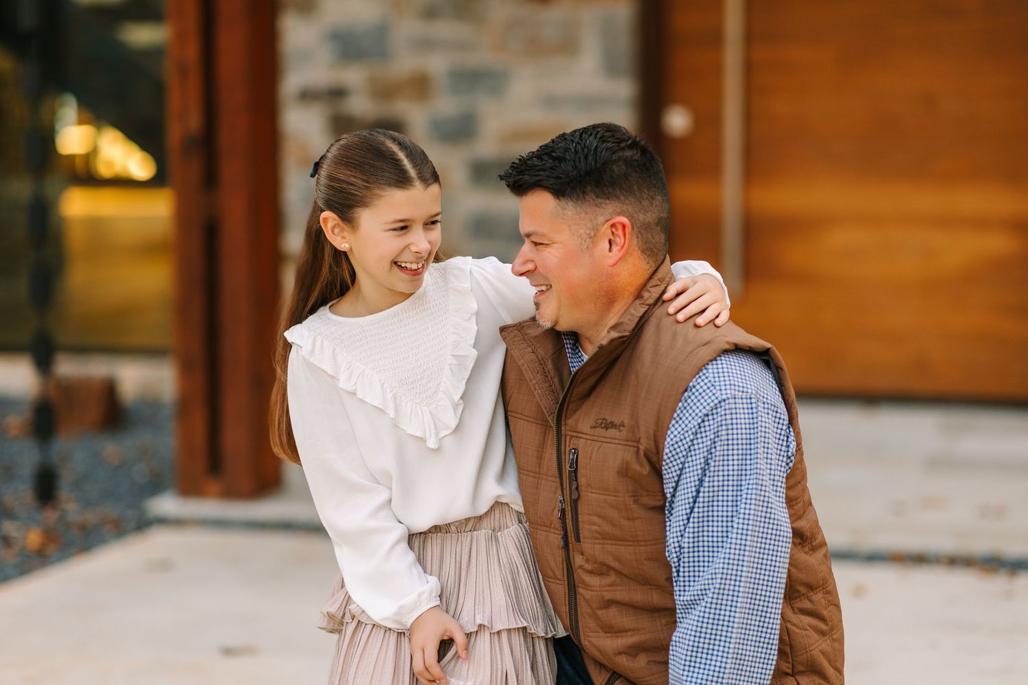 A couple in western apparel shares a romantic moment together on a sunny afternoon next to a rustic stone wall.