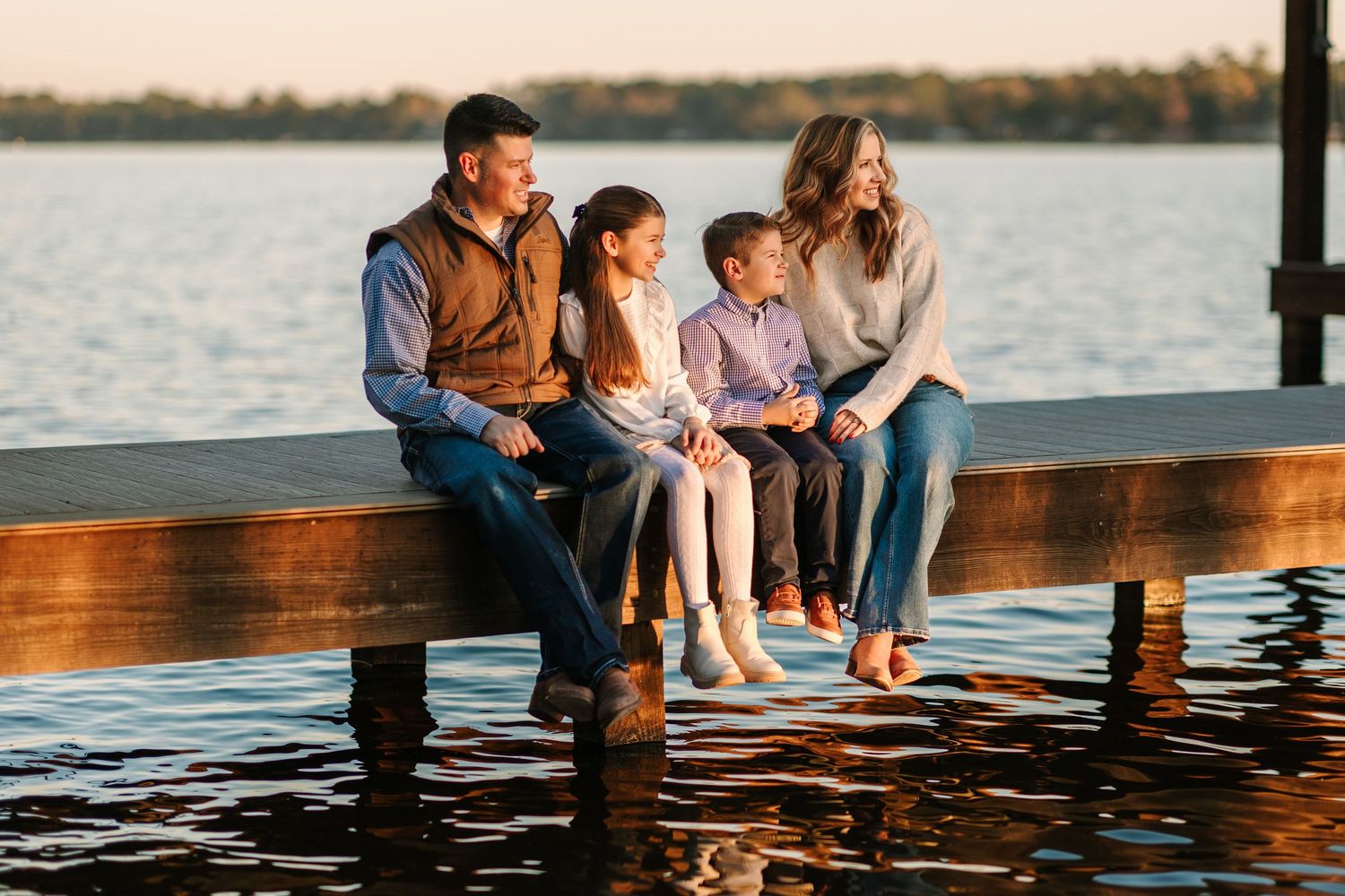 A family sits together on a wooden dock by the lake at sunset enjoying quality time outdoors.