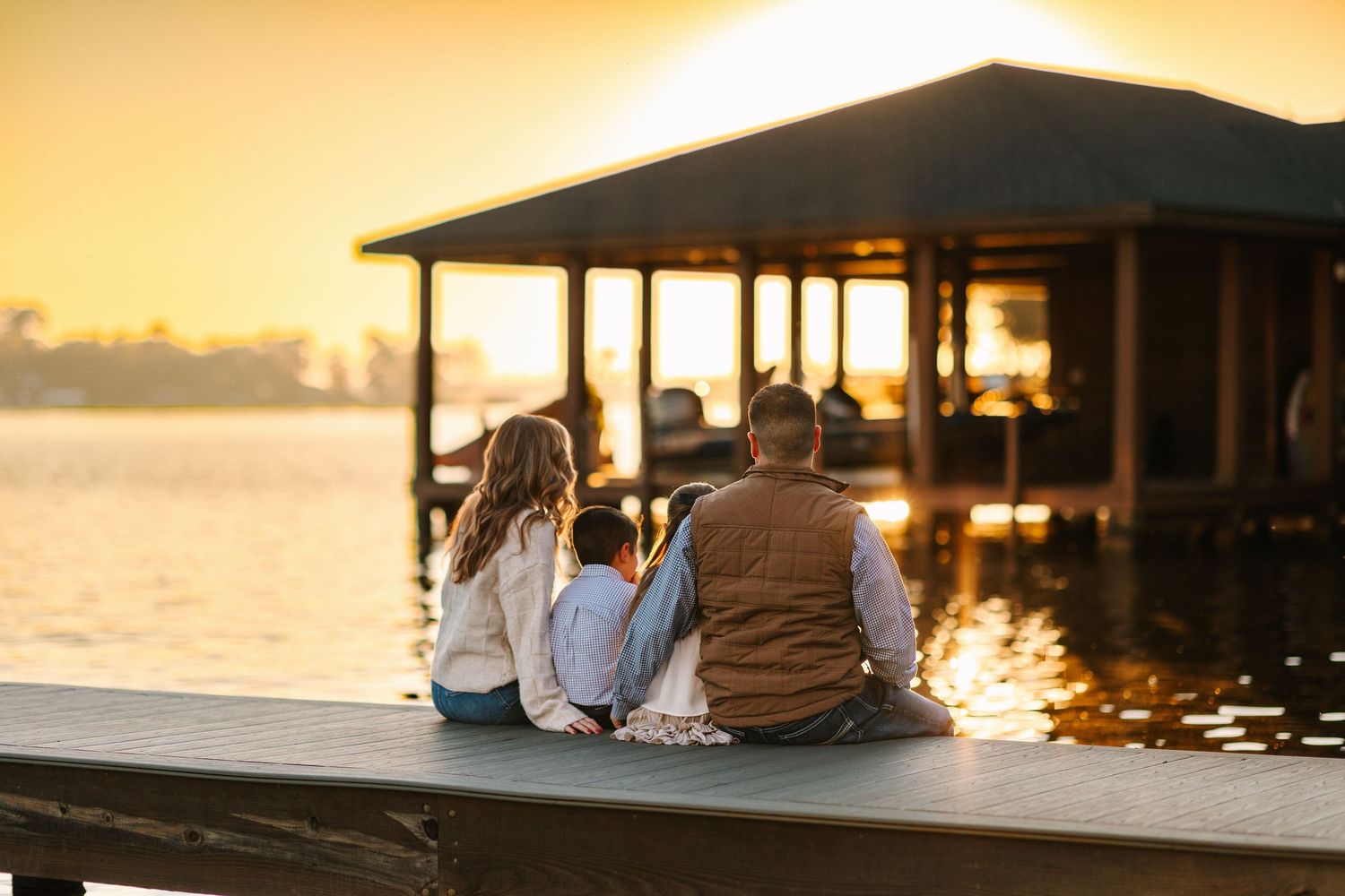 People sit together on wooden dock during peaceful sunset over waterfront.