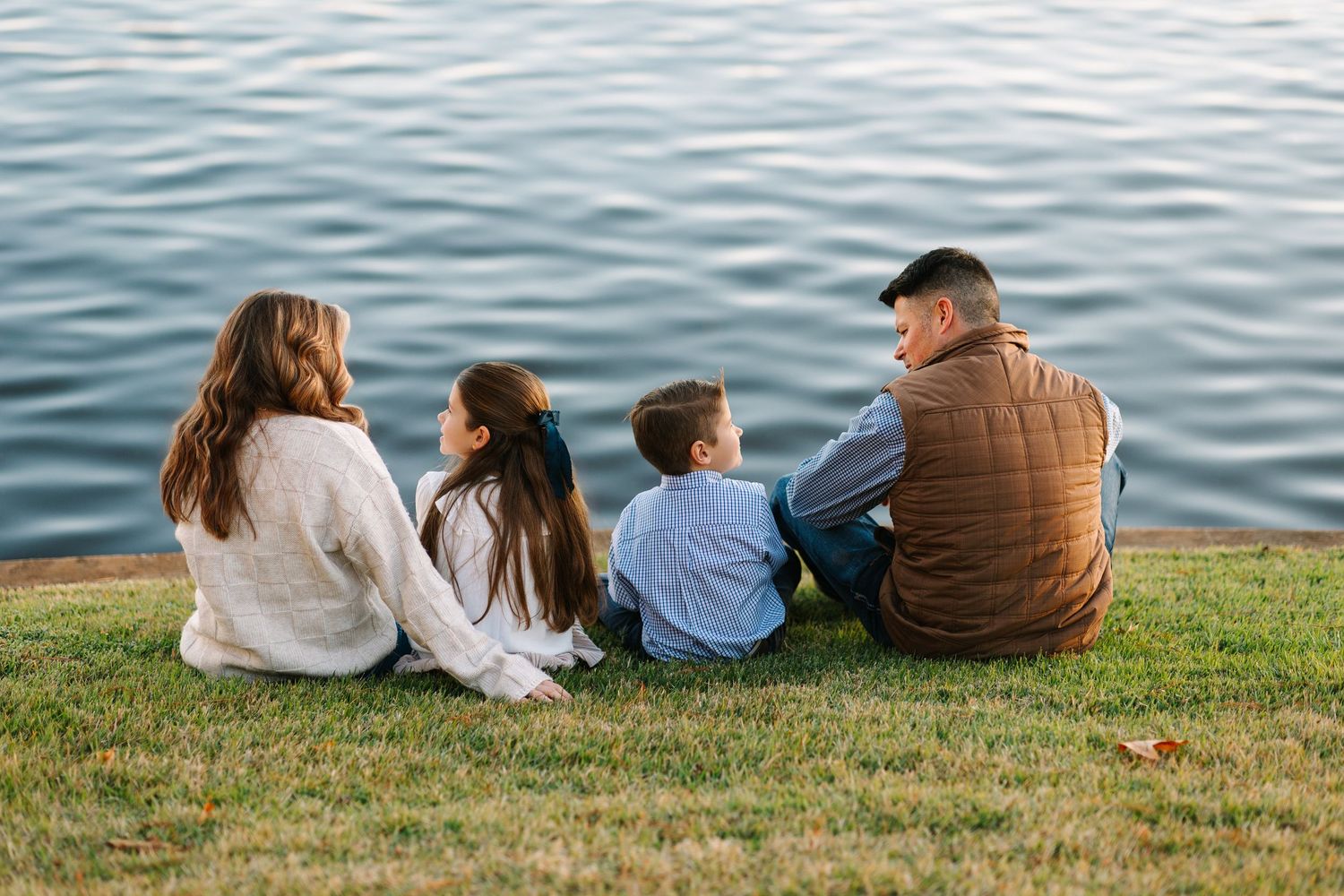 People sitting and relaxing on a grassy hill overlooking a serene body of water on a sunny day.