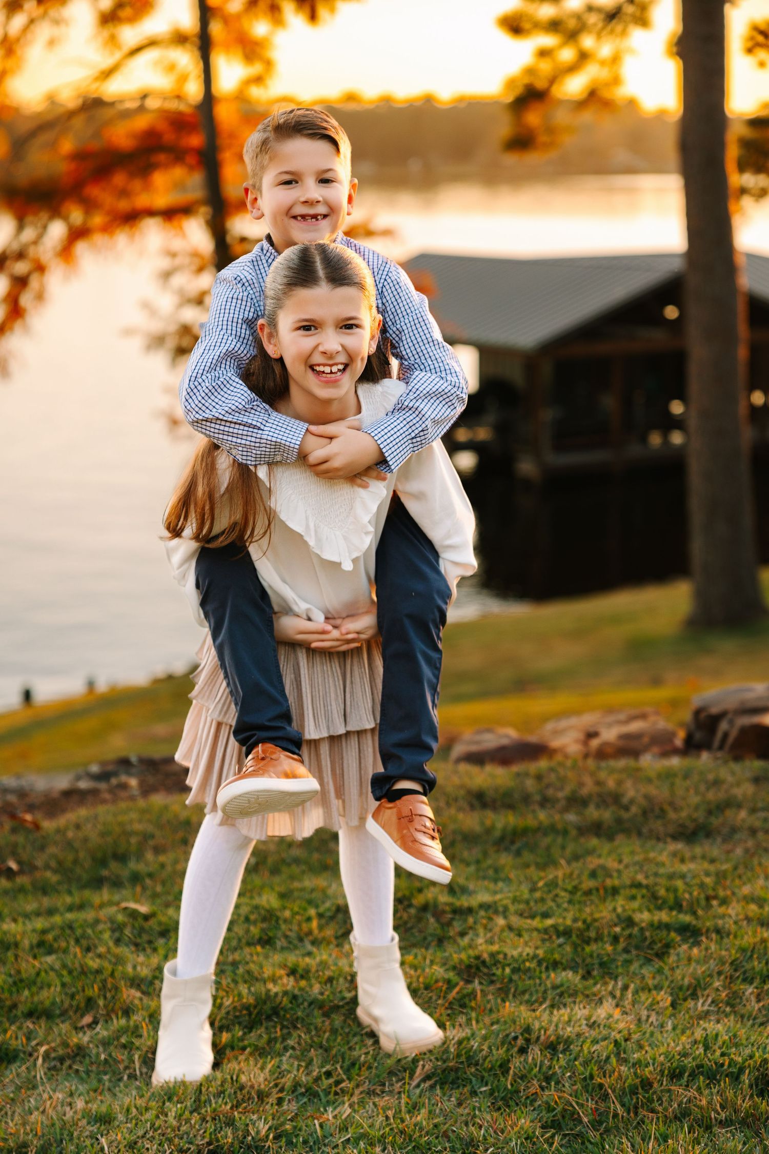Two children in casual clothing playfully posing together outdoors on a grassy hill during golden sunset.