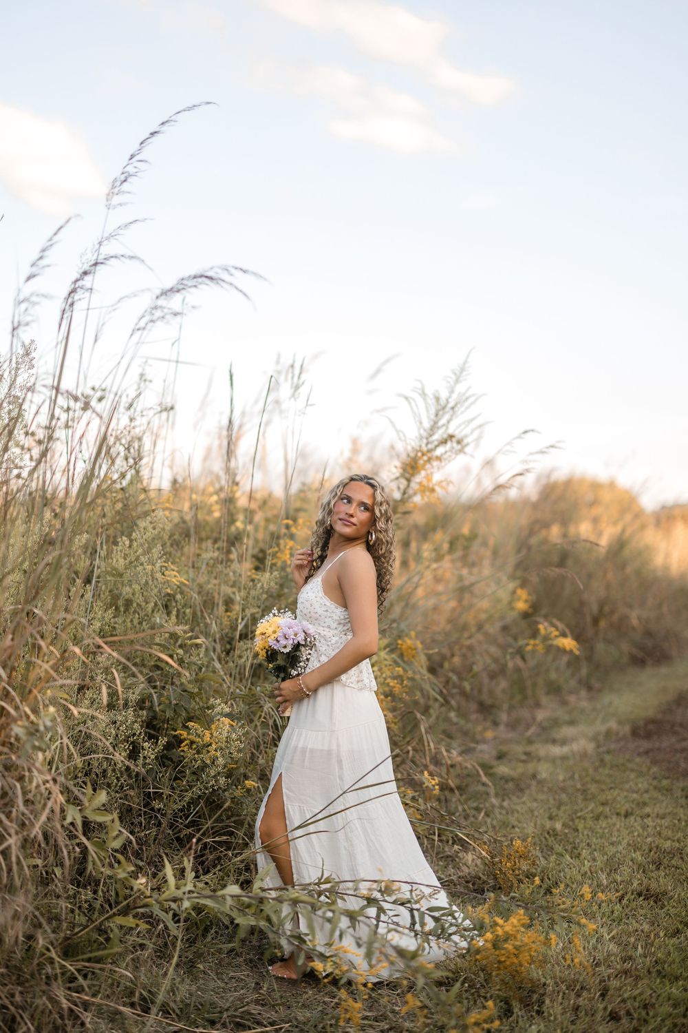 White wildflowers and tall grasses create a dreamy outdoor setting at sunset with a flowy white dress in focus.