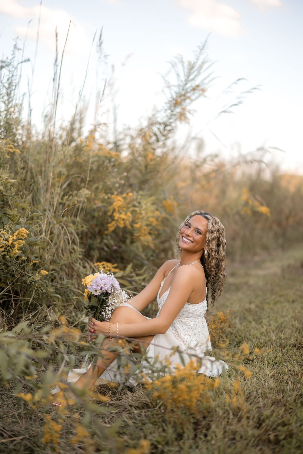 A person laughs joyfully while sitting among vibrant yellow wildflowers on a sunny fall day in a natural meadow setting.