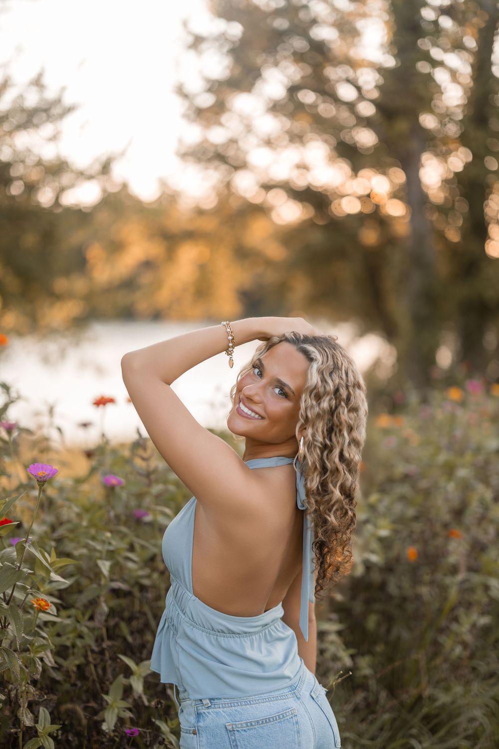 Woman posing playfully in a field of flowers during golden hour wearing blue overalls.