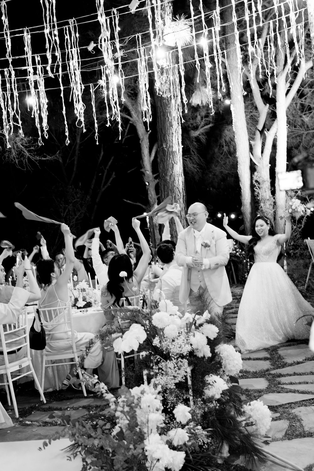 Black and white photo of bride and groom entering their outdoor evening wedding reception to cheering guests.