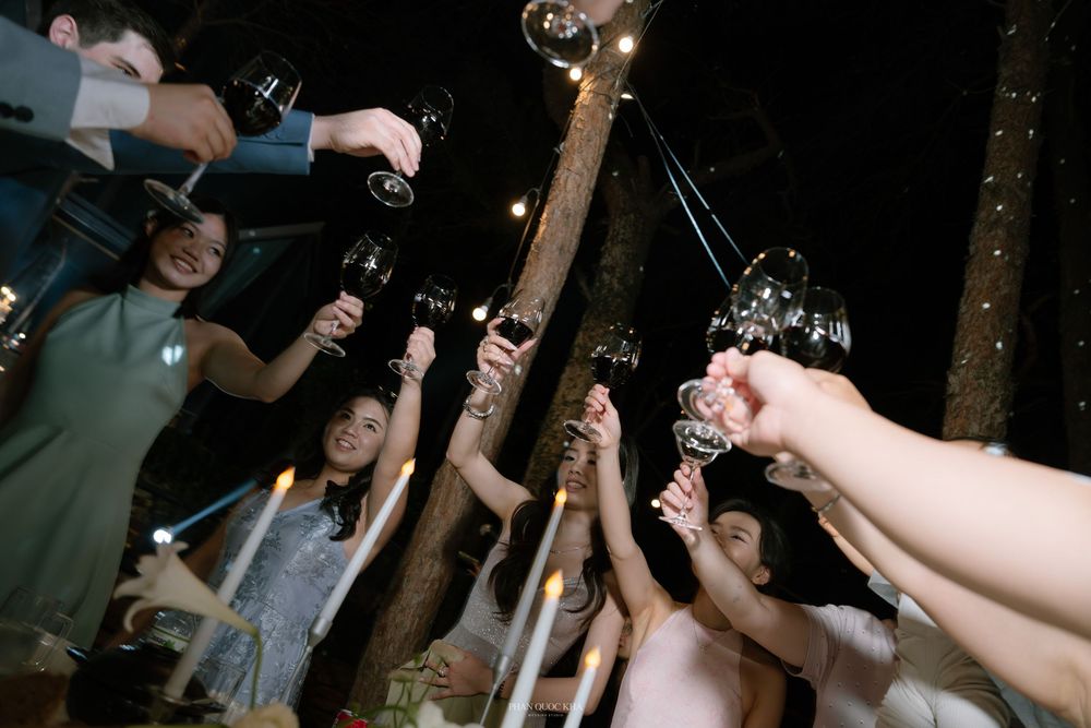 Wedding guests raise glasses of red wine and champagne for a festive toast at an outdoor night reception.
