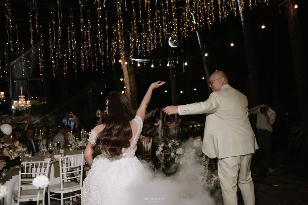 Bride and groom sharing first dance on fog-filled dance floor under hanging string lights.