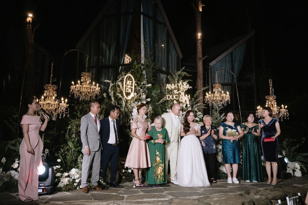Wedding party group photo at night in front of floral backdrop with chandeliers.