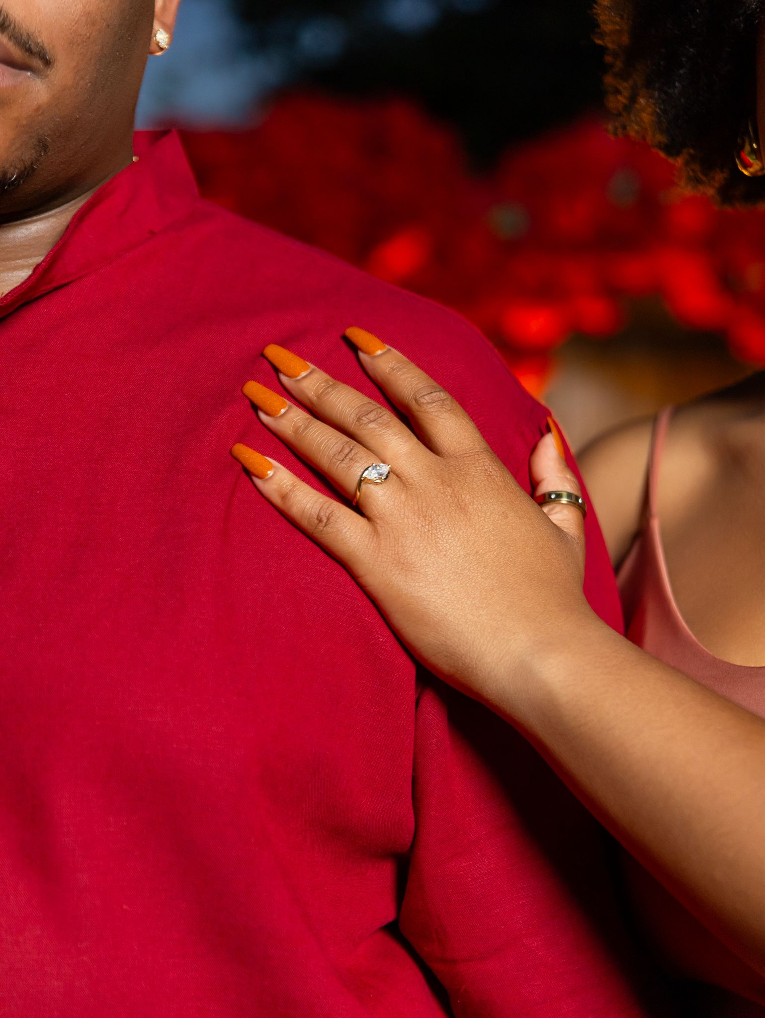 Close-up of a hand wearing an engagement ring against a red background.