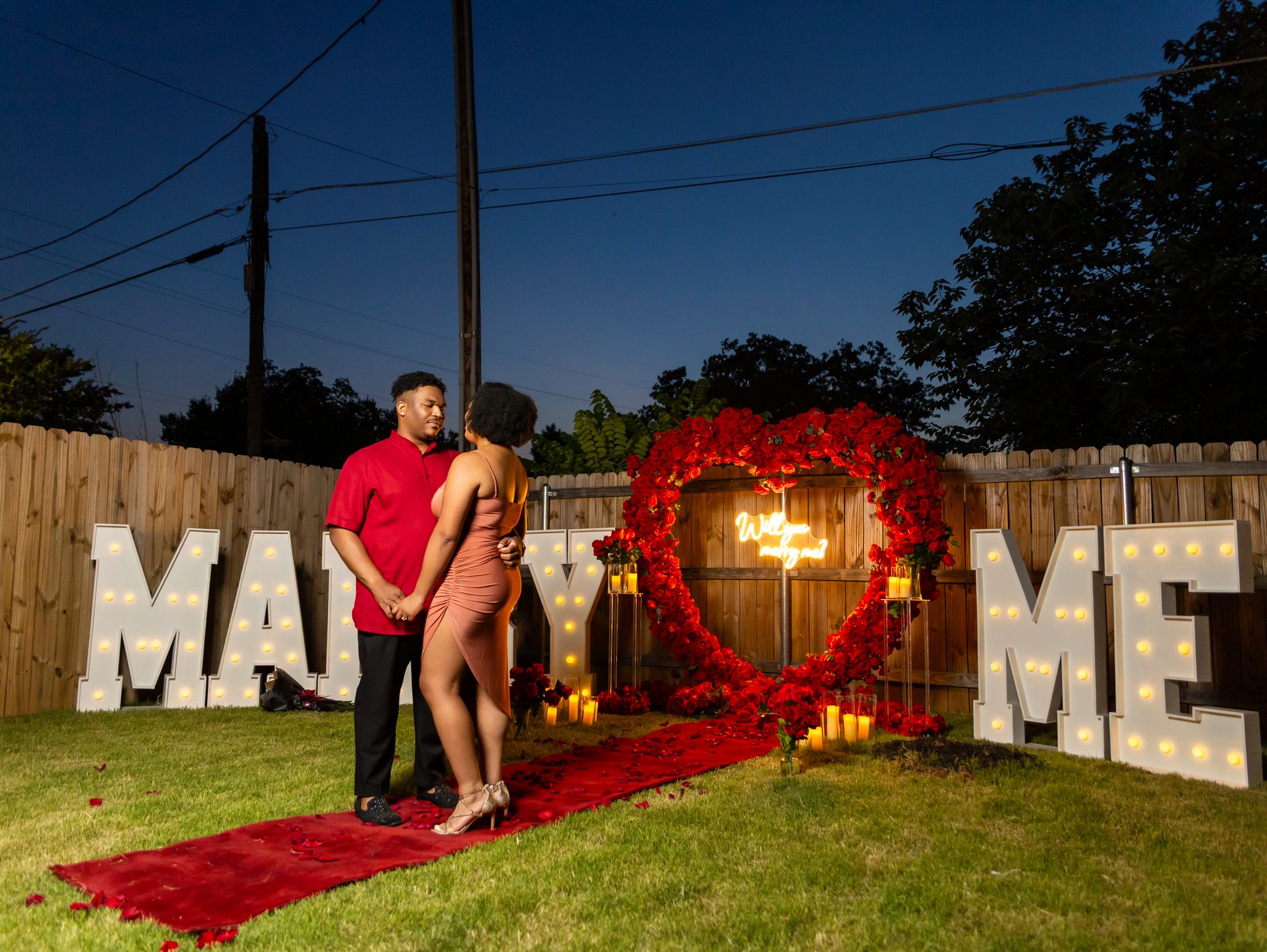 An outdoor proposal setup with illuminated letters and romantic decorations at dusk.