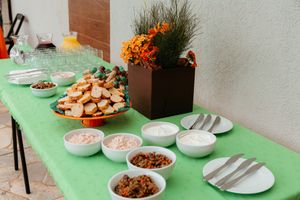 A long buffet table with a green tablecloth displays various dishes and serving platters at a party or gathering.