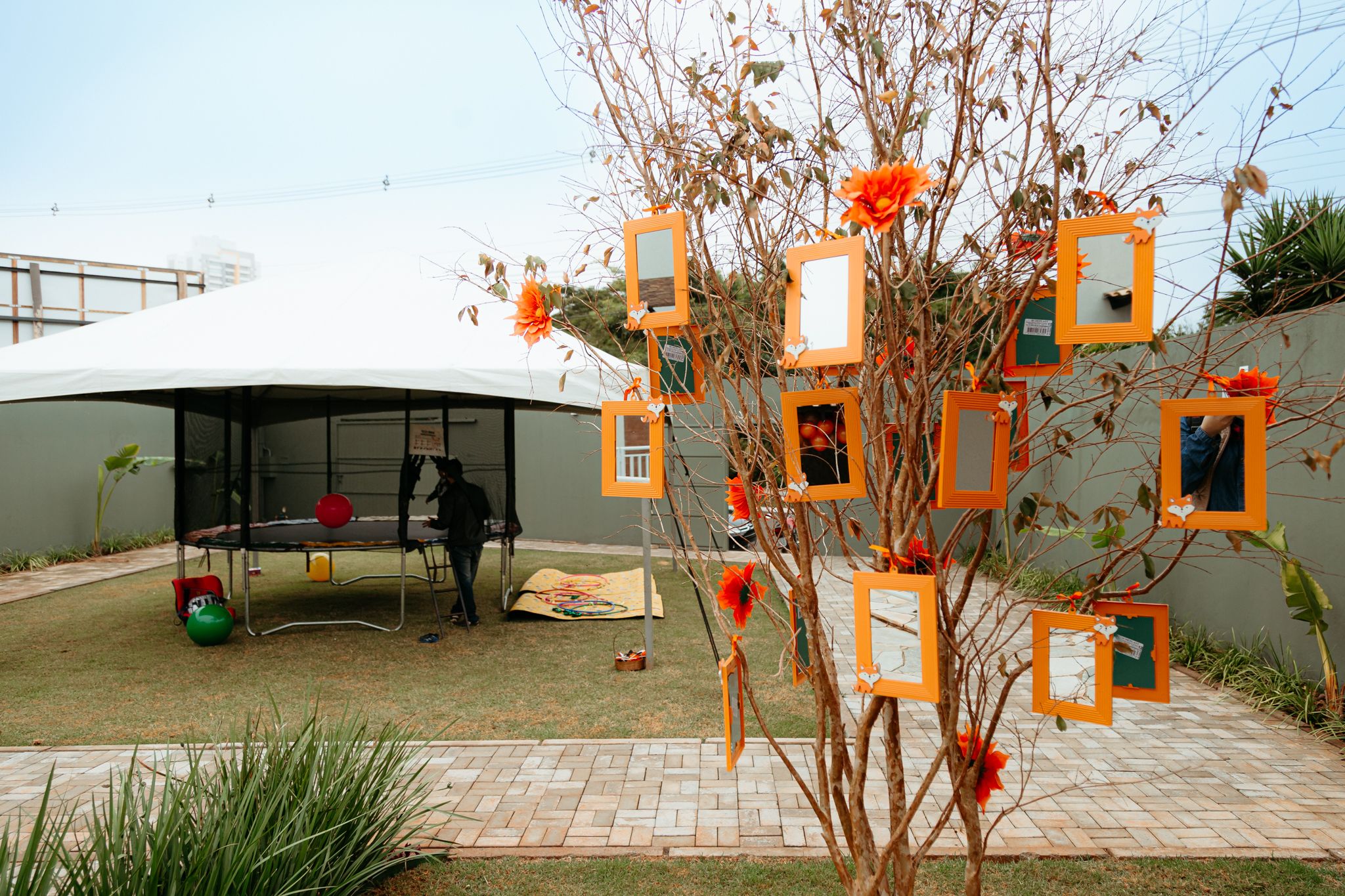 Decorative outdoor lanterns with orange candles hanging from bare tree branches against a cloudy sky.