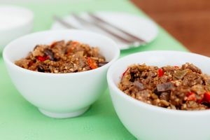 Bowls filled with crispy homemade granola clusters featuring nuts and dried fruits on a green surface.