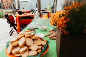 Party snacks and cookies arranged on orange plates with orange floral decorations on a green tablecloth.