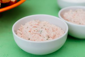 Creamy pink seafood dip or spread served in a small white ceramic bowl on a bright green surface.
