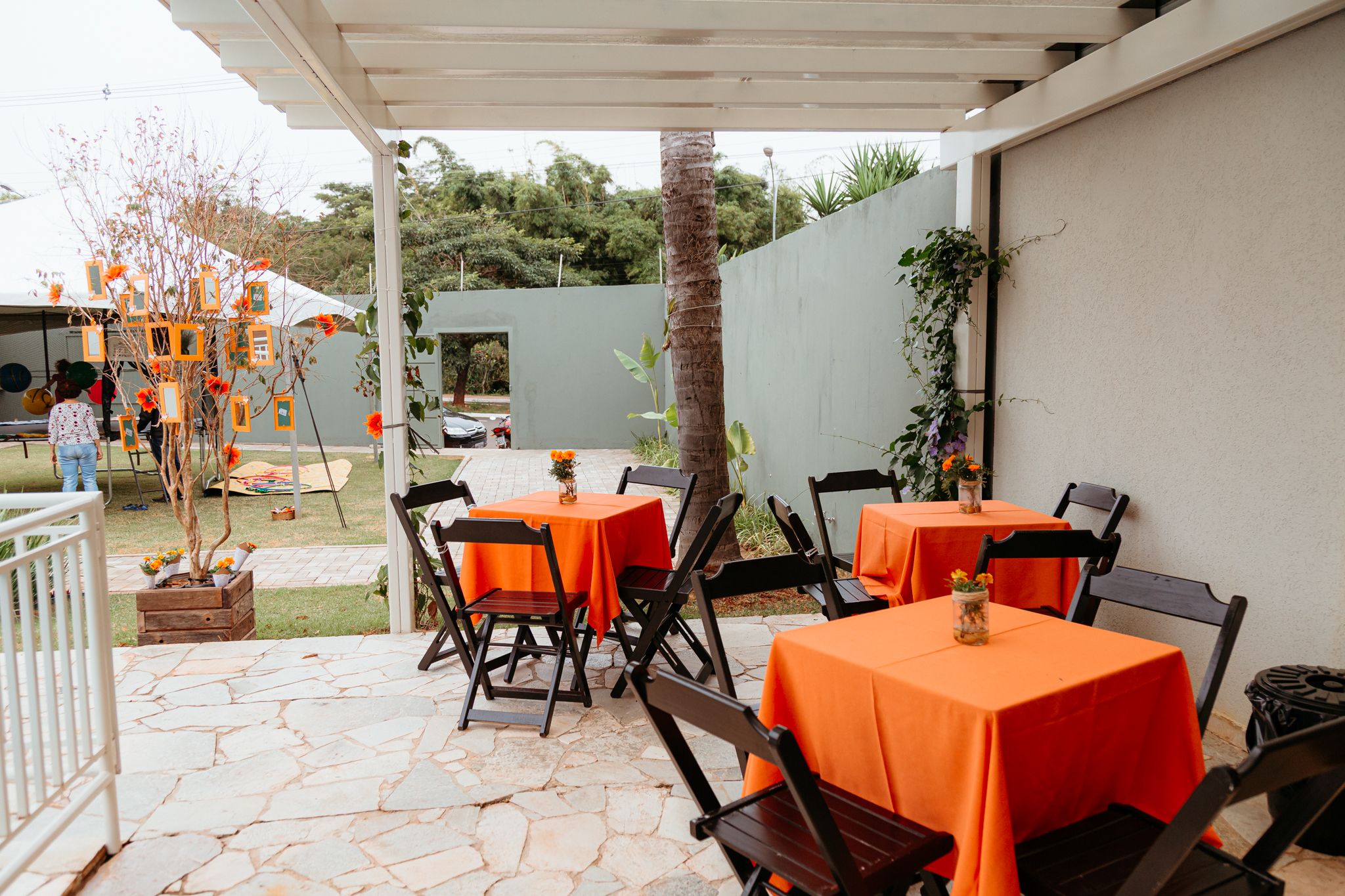 Outdoor event setup with bright orange tablecloths and chairs on a wooden patio in warm evening lighting.
